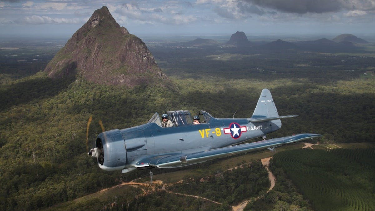 vintage warplane flying near glass house mountains, one of the popular moreton bay attractions for aviation and history enthusiasts